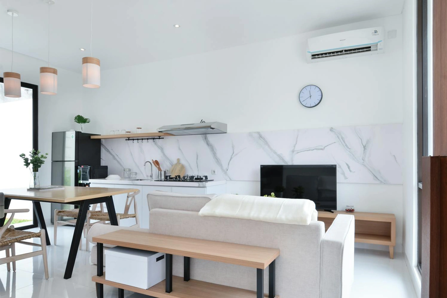 Modern living room and kitchen area with an air conditioner mounted on the wall, highlighting its role in maintaining a cool and comfortable indoor environment.