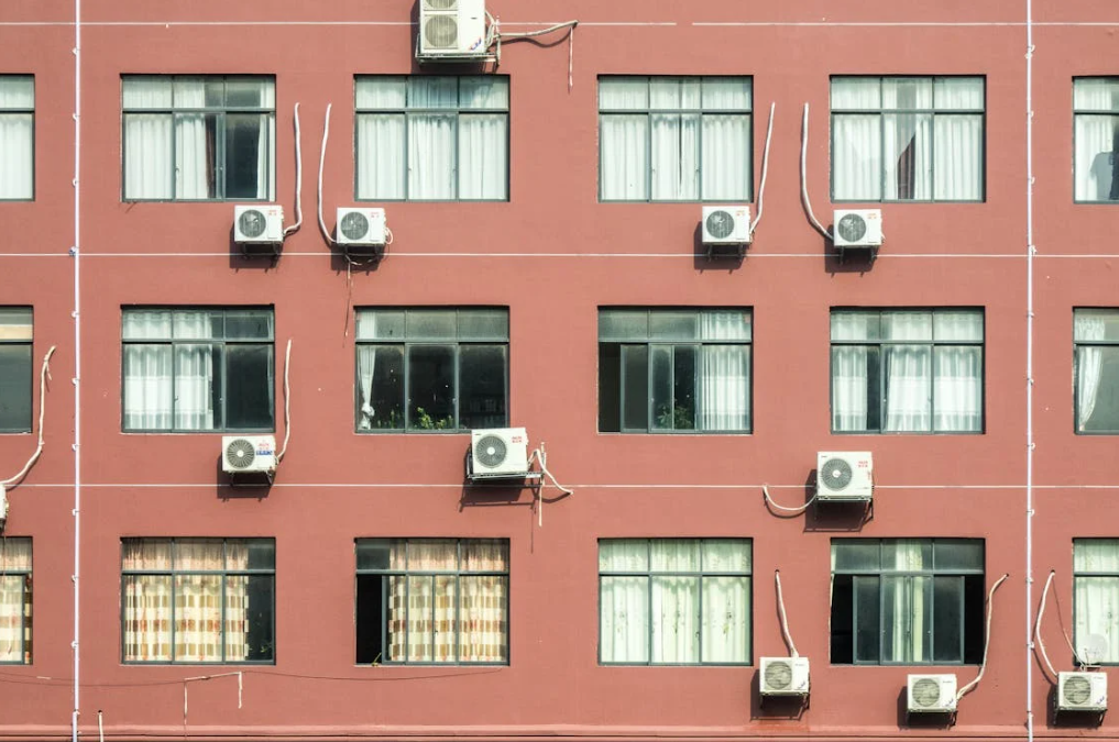 Exterior view of a building with several windows, each featuring an air conditioning unit mounted outside. The image highlights the importance of air filters in air conditioning systems, as they are essential in maintaining the efficiency and air quality provided by these units.